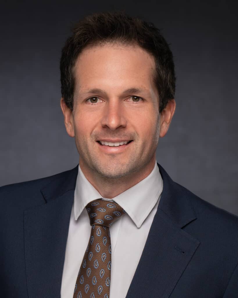 A professional headshot of a supply chain manager, featuring a confident individual in business attire, smiling warmly against a neutral background. The image conveys professionalism, approachability, and expertise in supply chain management.