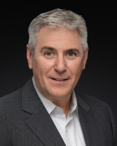 Professional headshot of an Aerospace Engineer team leader, dressed in business attire, exuding confidence and expertise, with a clean background highlighting their professional environment.