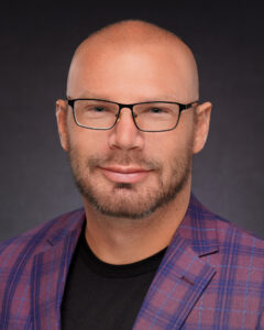 Professional headshot of Brandon Lee, a confident and approachable individual with a friendly smile. He is dressed in a smart, casual outfit, standing against a neutral background, exuding professionalism and warmth.