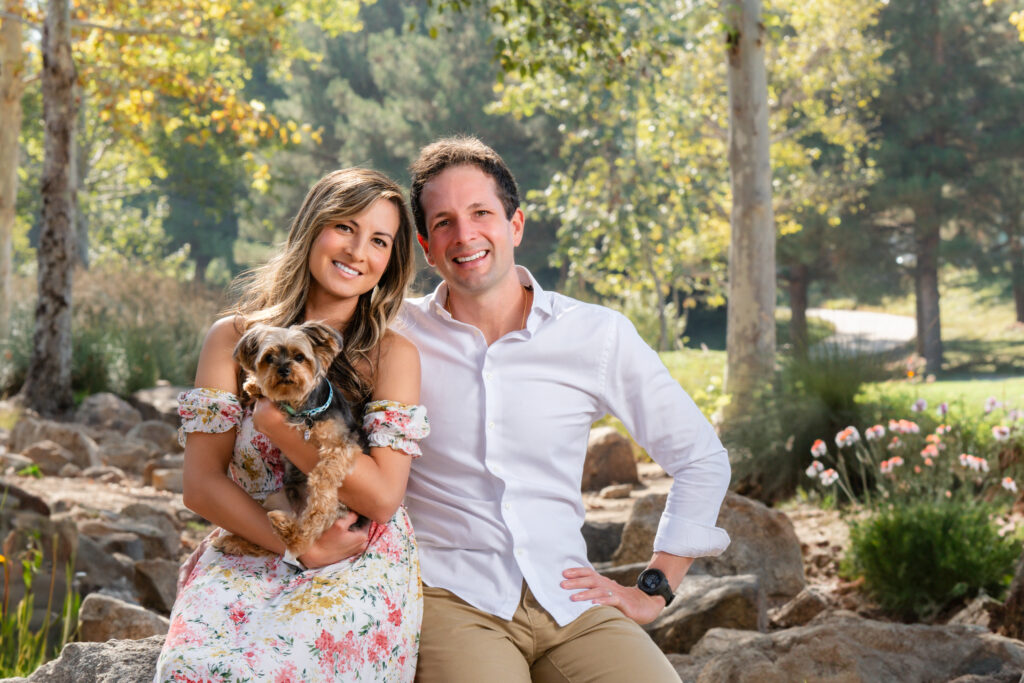 Outdoor lifestyle photo of a couple with their pet dog, smiling and enjoying a candid moment in a natural setting.